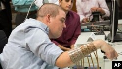 In this March 2016 photo provided by Ohio State University, Ian Burkhart plays a guitar video game as part of a study with neural bypass technology at The Ohio State University Wexner Medical Center in Columbus. A computer chip in Burkhart's brain reads h