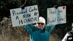 A person holds signs as the hearse containing the casket of former President Jimmy Carter, pauses at the Jimmy Carter Boyhood Farm in Archery, Ga., Jan. 4, 2025. Carter died Dec. 29 at the age of 100.