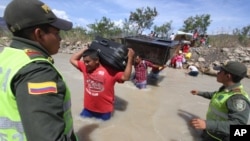 En esta foto de archvio se ven policías colombianos observando a venezolanos cruzando el río Táchira desde Venezuela con sus pertenencias al hombro.