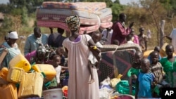 FILE - Refugees who fled the recent violence in South Sudan and crossed the border into Uganda carry their belongings as they await transportation from a transit center in the town of Koboko to a nearby settlement in Arua District, in northern Uganda, Jan 6, 2014.