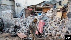 FILE - A soldier walks past wreckage after an attack on the Afrik hotel in Mogadishu, Somalia, Feb. 1, 2021. Though security forces eventually ended the attack, Somalia's government warned on Saturday that anyone who pays extortion money to al-Shabab would face legal action.