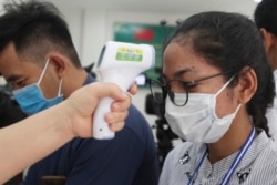 FILE - A local journalist, right, has her temperature checked to cover a handover ceremony of a donation in Phnom Penh, Cambodia, Saturday, March 28, 2020. Cambodia on Saturday held the ceremony to receive a donation from Alibaba and Jack Ma foundation of its 20,000 COVID-19 test kits for prevention, control and response to the new coronavirus in Cambodia. (AP Photo/Heng Sinith)
