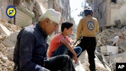 In this picture provided by the Syrian Civil Defense group known as the White Helmets, residents sit amongst rubble in rebel-held eastern Aleppo, Syria, Oct. 11, 2016.