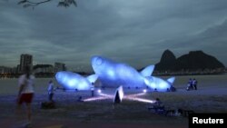 Seorang wanita melintasi ikan raksasa yang terbuat dari botol plastik dan dipamerkan di Pantai Botafogo, Rio de Jenairo (19/6). Konferensi Pembangunan yang Berkelanjutan PBB Rio +20 akan berlangsung di kota ini dari tanggal 20 hingga 22 Juni 2012.