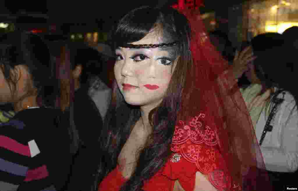 A woman who drew part of a face on her cheek, stands among the crowd at a costume party to celebrate Halloween in Wuhan, Hubei province, China, Oct. 31, 2013.