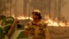 A Forest Corporation worker manages a fire hose as he battles a fire near Moruya, Australia, Jan. 4, 2020. Australia's Prime Minister Scott Morrison called up about 3,000 reservists as the threat of wildfires escalated Saturday in at least three states.