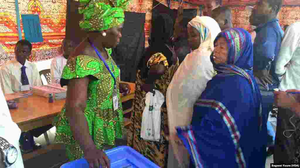 Une Tchadienne se fait aider à placer son bulletin dans l'urne à côté d'autres électeurs qui attendent dans un bureau de vote à N'Djamena, Tchad, 10 avril 2016. (VOA/Bagassi Koura)