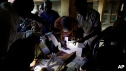 Petugas pemilu menggunakan cahaya dari ponselnya untuk mempersiapkan kertas suara bagi pemilih yang proses akreditasinya tertunda di salah satu TPS di Kaduna, Nigeria (28/3). (AP/Jerome Delay)