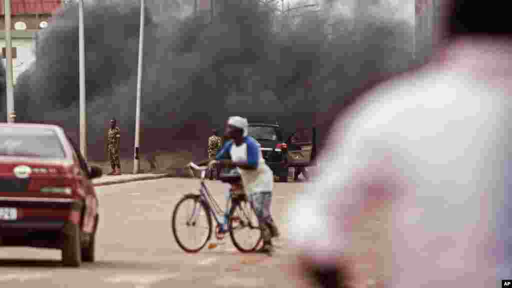 La fumée s'élève pendant que des troupes du Burkina Faso, à l'arrière-plan, débarrassent les débris d'une route où des protestataires opposés au coup d'Etat ont érigé des barricades à Ouagadougou, Burkina Faso, 18 septembre 2015.