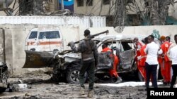 Seorang petugas polisi berjaga-jaga saat pekerja Bulan Sabit Merah mengeluarkan jenazah korban di lokasi ledakan bom mobil di Mogadishu, Somalia, 25 September 2021. (Foto: Reuters)