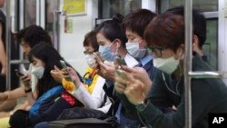 Passengers wear masks as a precaution against Middle East Respiratory Syndrome (MERS) as they use their smartphones on a subway train in Seoul, South Korea, Monday, June 8, 2015. 