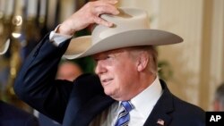 FILE - President Donald Trump tries on a Stetson hat during a "Made in America," product showcase featuring items created in each of the U.S. 50 states, at the White House, in Washington, July 17, 2017.