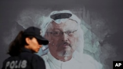 FILE - A Turkish police officer walks past a picture of slain Saudi journalist Jamal Khashoggi prior to a ceremony, near the Saudi Consulate in Istanbul, marking the one-year anniversary of his death, Oct. 2, 2019.