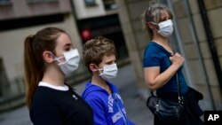 A family wearing face mask to protect of the coronavirus go for a walk, in Pamplona, northern Spain, Sunday, April 27, 2020. On Sunday, children under 14 years old will be allowed to take walks with a parent for up to one hour and within one…