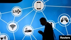 A man looks at his phone in front of a stand at the Mobile World Congress in Barcelona, Spain, showing a variety of devices connected via Wi-Fi and Internet of Things networks, Feb. 28, 2017
