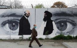 FILE - An Afghan man walks past a wall painted with photo of Zalmay Khalilzad, U.S. envoy for peace in Afghanistan, and Mullah Abdul Ghani Baradar, the leader of the Taliban delegation, in Kabul, Afghanistan, April 13, 2020