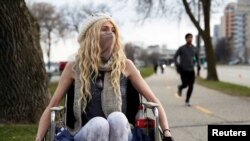 FILE - Colleen Curtin, who says she is suffering from health issues that she has not been able to get diagnosed by testing due to the COVID-19 pandemic, sits in her wheelchair for a portrait along a path in Madison, Wisconsin, April 17, 2020.