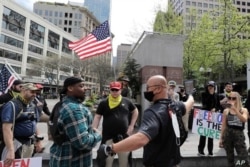 Miembros de un grupo que usaban camisetas con el logo del grupo de ultraderecha Proud Boys discuten con contramanifestantes sobre las órdenes estatales de Washington de permanecer en casa.