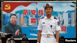 在香港海軍基地，一名中國水兵站在一面具有中共黨旗、習近平像和香港景象的大型看板前面（2017年7月8日）。