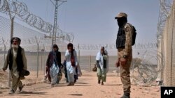 FILE - In this Aug. 20, 2021, photo, Pakistani army soldier stands guard while Afghan people enter into Pakistan through a border crossing point, in Chaman, Pakistan.