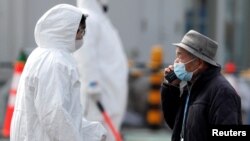 穿上防護服的工作人員協助鑽石公主號的乘客離船。