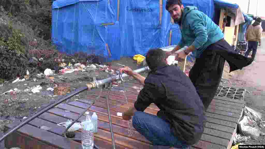Deux migrants afghans se lavent les mains dans la "jungle". Ce camp est situé aux abords de Calais dans le nord de la France, 13 octobre 2015 (Nicolas Pinault/VOA).
