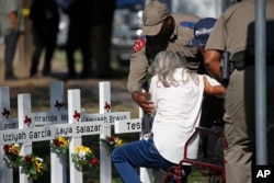 Polisi membantu seorang perempuan setelah dia memberi hormat di depan salib dengan nama anak-anak yang terbunuh di luar Sekolah Dasar Robb di Uvalde, Texas Kamis, 26 Mei 2022. (Foto: AP)