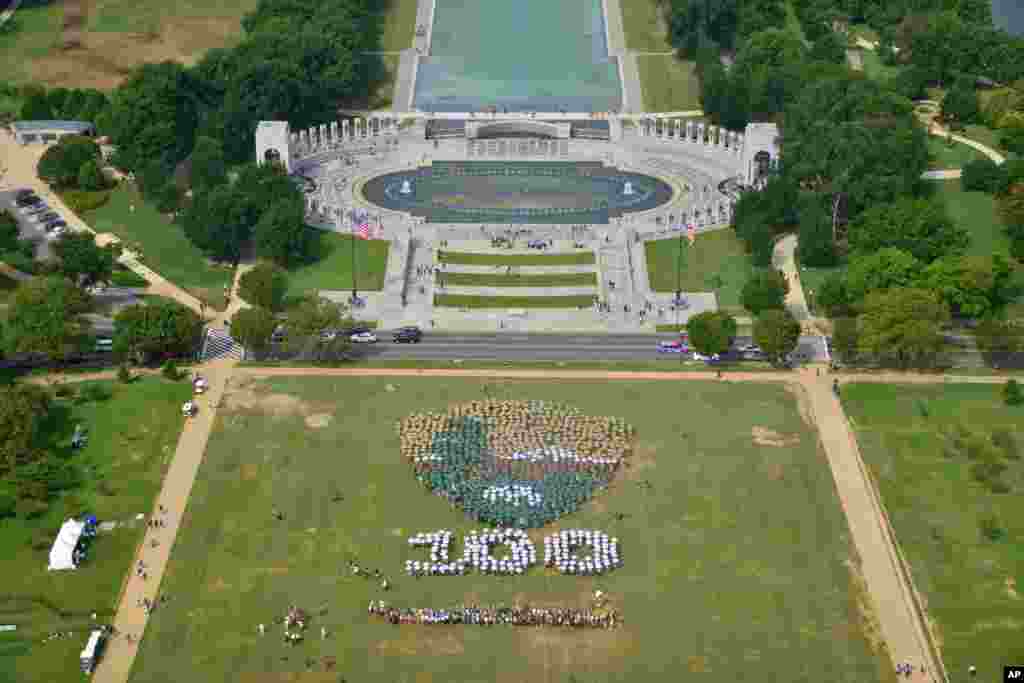 People on the National Mall in Washington, looking toward the World War II Memorial, Aug. 25, 2016, recreate a giant, living version of the National Park Service emblem, using brown, green and white umbrellas.