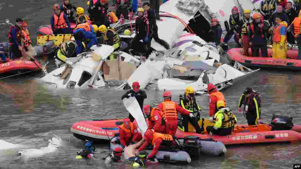 Rescue personnel in a rubber dinghy lift a passenger (bottom C) from the waters around the wreckage of a TransAsia ATR 72-600 turboprop plane that crash-landed into the Keelung river outside Taiwan's capital Taipei in New Taipei City.