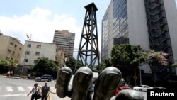 Archivo - Personas caminan frente a una escultura frente al edificio de PDVSA en Caracas, Venezuela, 