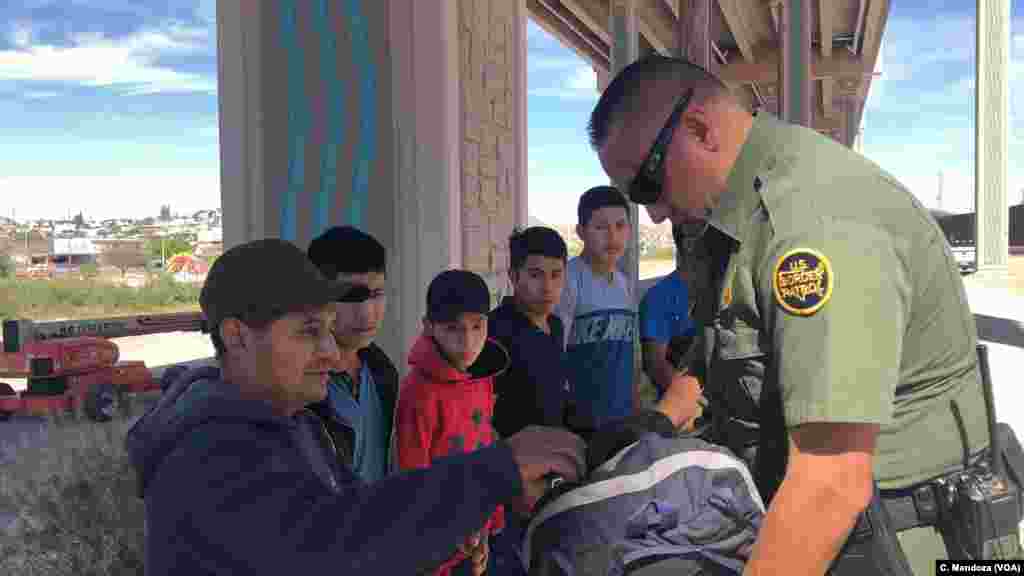 U.S. Customs and Border Patrol agents check migrants' belongings. This group of Guatemalan migrants, which includes a child, wait to be processed by an agent, April 9, 2019. C. Mendoza/VOA News