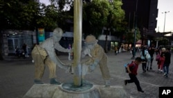 Un niño salta cerca de la escultura "Los Petroleros" que muestra a dos hombres trabajando en un taladro petrolero de Petróleos de Venezuela, S.A, PDVSA, en el bulevar Sabana Grande, en Caracas, Venezuela, el 20 de marzo de 2023. (Foto AP/Ariana Cubillos)
