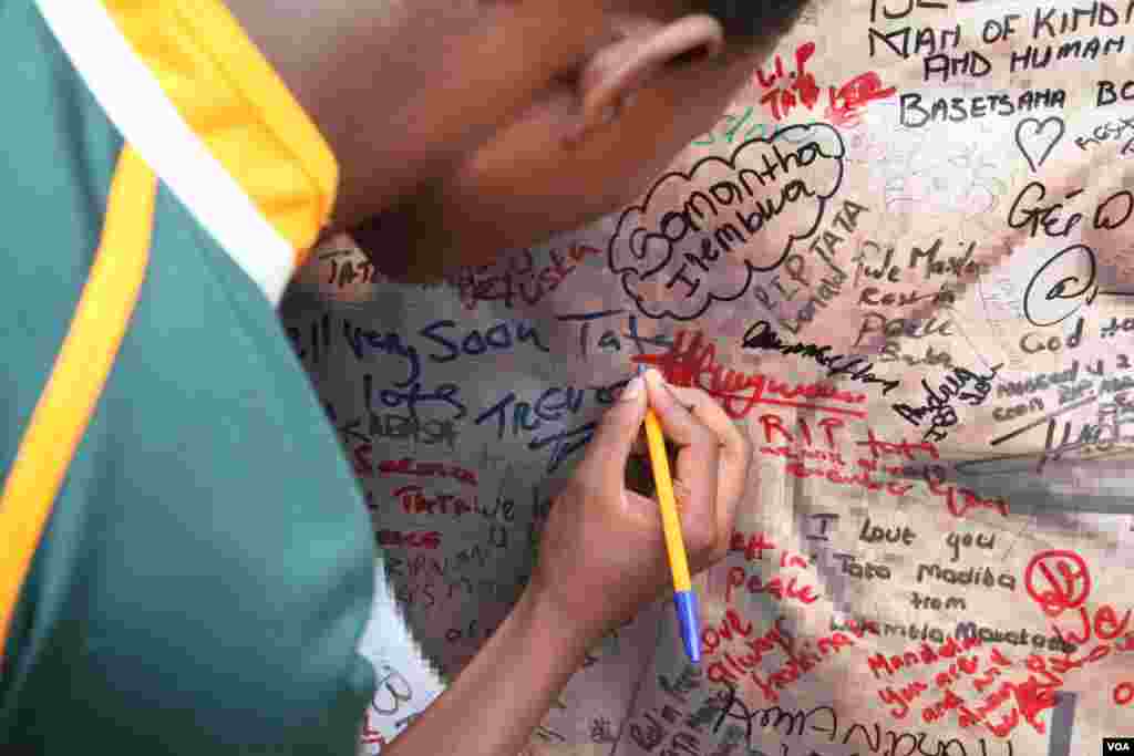 Um jovem escreve o seu nome num poster de Mandela à porta de sua casa em Soweto, África do Sul.(Hannah McNeish para VOA)