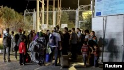 Refugees and migrants stand at the closed gate of the Moria migrant camp, after a fire at the facility, on the island of Lesbos, Greece, Sept. 19, 2016. 