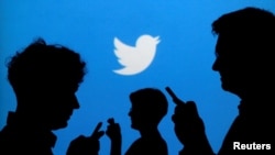 FILE - People holding mobile phones are silhouetted against a backdrop projected with the Twitter logo, Sept. 27, 2013. 