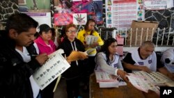 An election worker hands a ballot to a voter as observers from political parties mark off each voter from copies of the rolls in Chimalhuacan, Mexico state, June 4, 2017.