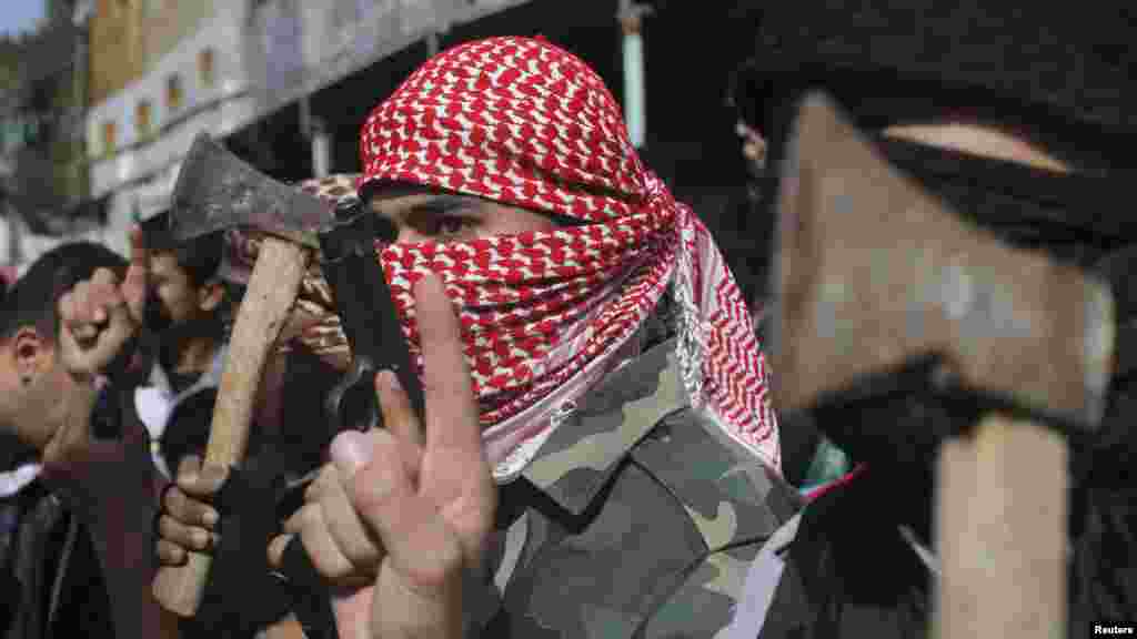 Masked Palestinians hold axes and a gun as they celebrate with others an attack on a Jerusalem synagogue, in Rafah in the southern Gaza Strip, Nov. 18, 2014.
