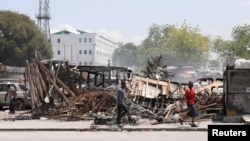 ARCHIVO - Personas caminan cerca del palacio presidencial junto a restos de vehículos incendiados por pandillas, mientras la violencia se extiende y las pandillas armadas amplían su control sobre la capital, en Puerto Príncipe, el 25 de marzo de 2024.