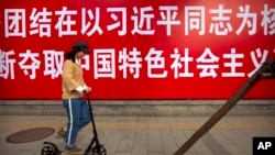 资料照：一名女子滑着踏板车路过北京街头的一条政治标语。（2017年10月12日）