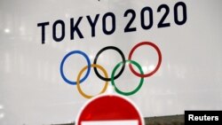 東京街頭交通警示牌後的東京奧運會旗幟。（2020年3月23日）