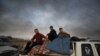 A man and two boys sit on belongings at the back of a truck as they flee Ras al-Ayn, Syria, Oct. 9, 2019, with smoke billowing in the background during a Turkish offensive.