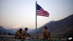 FILE - In this Sept. 11, 2011 photo, US soldiers sit beneath an American flag just raised to commemorate the tenth anniversary of the 9/11 attacks at Forward Operating Base Bostick in Kunar province, Afghanistan. 