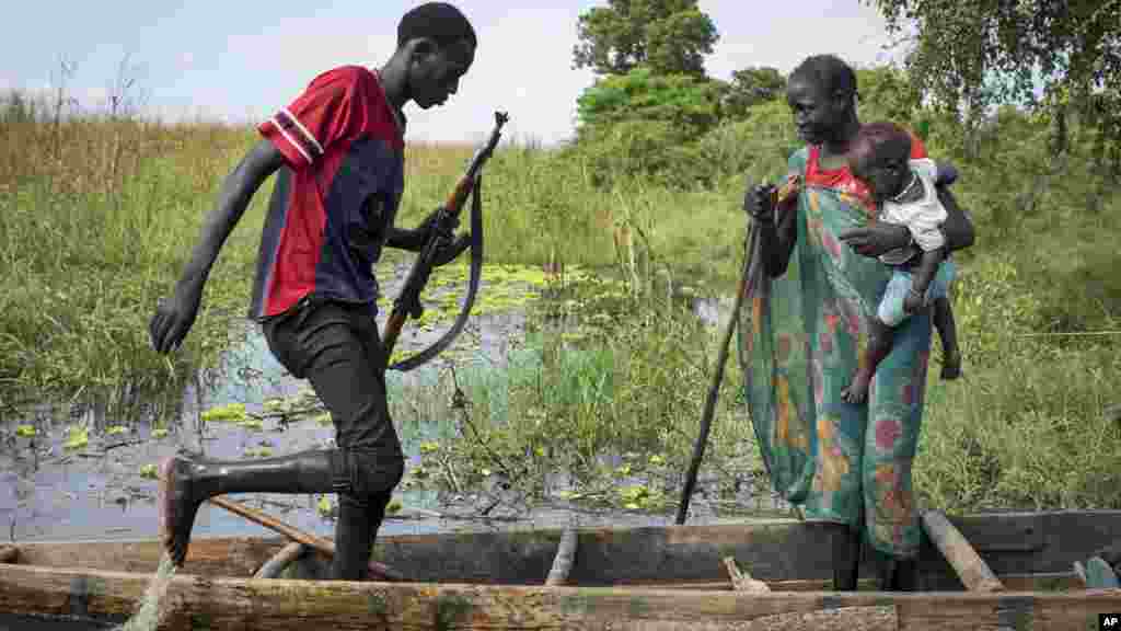 Une femme et un enfant de l’ethnie Nuer et un rebelle montent sur une pirogue au milieu des marécages, près d’un camp des déplacés inondé à Bentiu, Soudan du Sud, 20 septembre 2014. (AP Photo/Matthew Abbott)