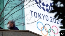 A man wearing a protective mask to help curb the spread of the coronavirus walks near the banner for the Tokyo 2020 Olympic Games Thursday, Feb. 25, 2021, in Tokyo. The Japanese capital confirmed more than 340 new coronavirus cases on Thursday. (AP…