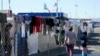 Migrantes caminan junto a la cerca de un campamento improvisado que bloquea la entrada a un cruce peatonal a Estados Unidos (arriba), el 8 de noviembre de 2021, en Tijuana, México. 