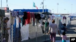 Migrantes caminan junto a la cerca de un campamento improvisado que bloquea la entrada a un cruce peatonal a Estados Unidos (arriba), el 8 de noviembre de 2021, en Tijuana, México. 