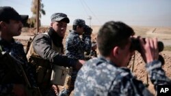 Iraqi federal police officers look towards Islamic State group territory as civilians flee the area, in the town of Albu Saif, Iraq, Feb. 21, 2017. A military spokesman says Iraqi forces are consolidating their gains south of Mosul ahead of moving deeper into the city's Islamic State-held western half.