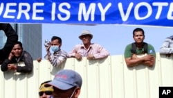 Cambodian workers look through a partition of a construction site below a banner which reads "Where is my vote" as supporters of opposition Cambodia National Rescue Party gather in Phnom Penh, Cambodia, Saturday, Sept. 7, 2013.