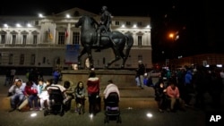Residents sent running into the street after a magnitude-8.3 earthquake sit next to an equestrian statue in the main square of Santiago, Chile, Sept. 16, 2015.