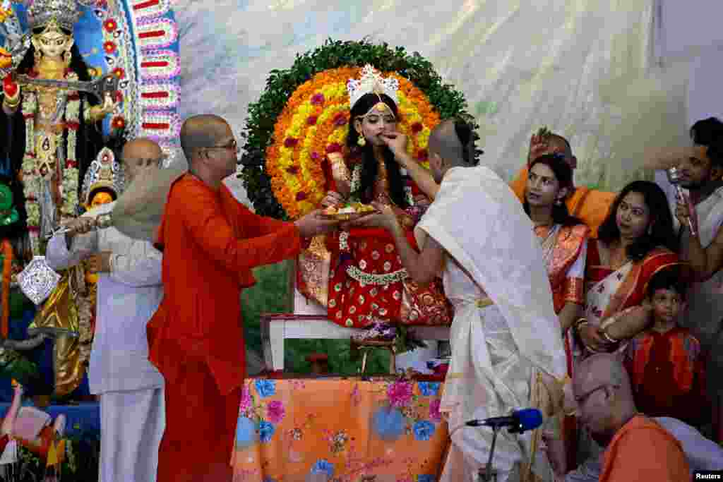 Hindu priests offer sweets to a young girl dressed as "Kumari" who is worshipped during the Durga Puja festival, at a temple in Dhaka, Bangladesh.